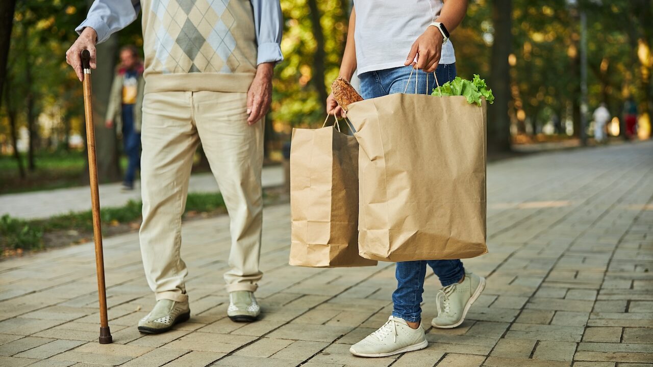 woman helping elderly man carry groceries