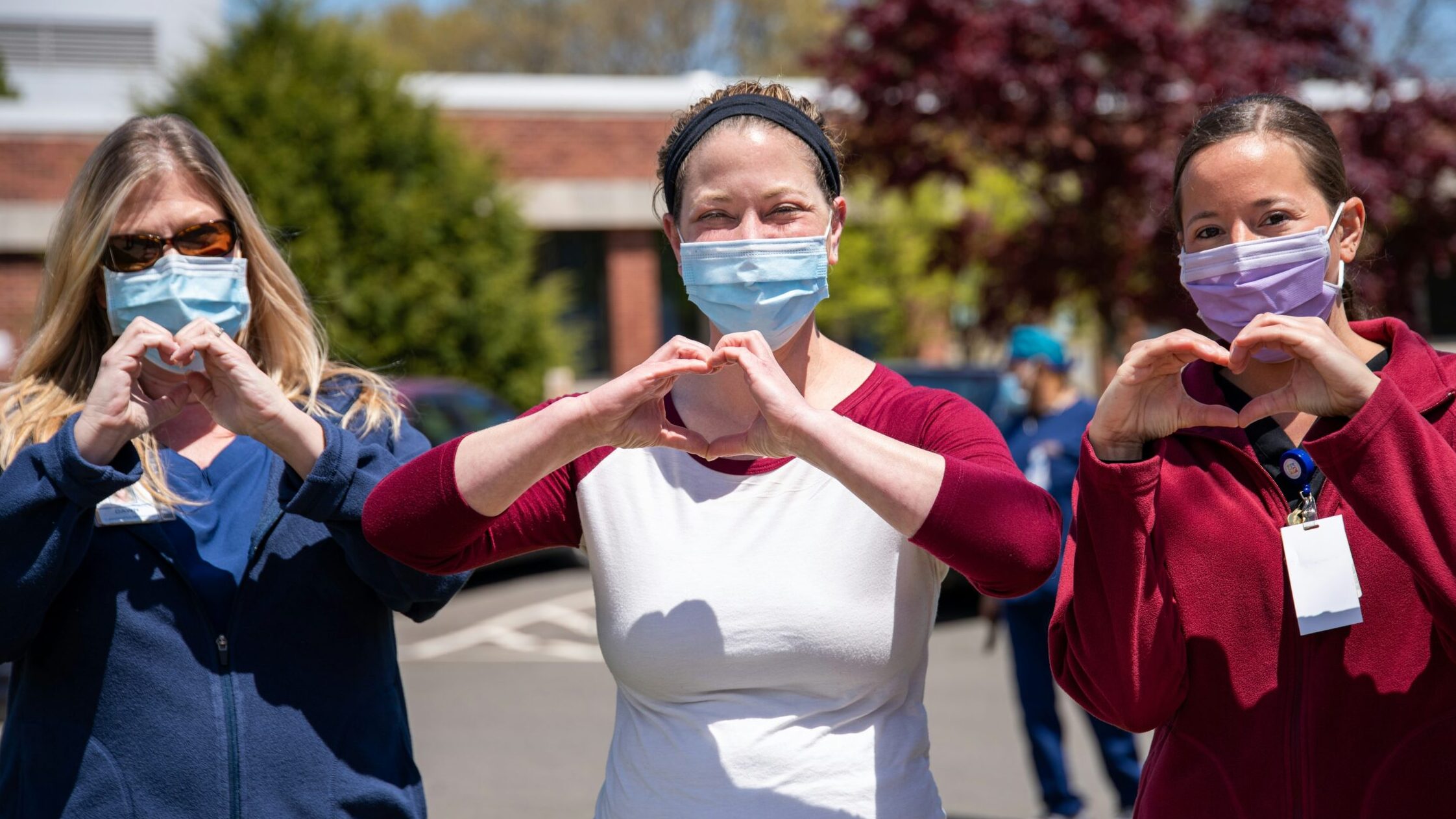 Three healthcare workers hold up their hands to look like hearts.