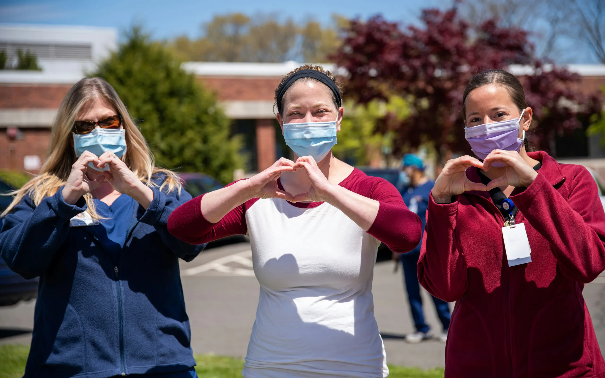 Three healthcare workers hold up their hands to look like hearts.